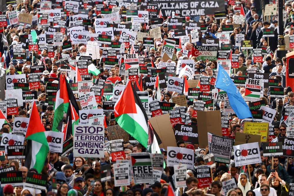 An image of a crowd of demonstrators protesting in solidarity with Palestinians in Gaza. Many fly Palestinian flags and hold placards.
