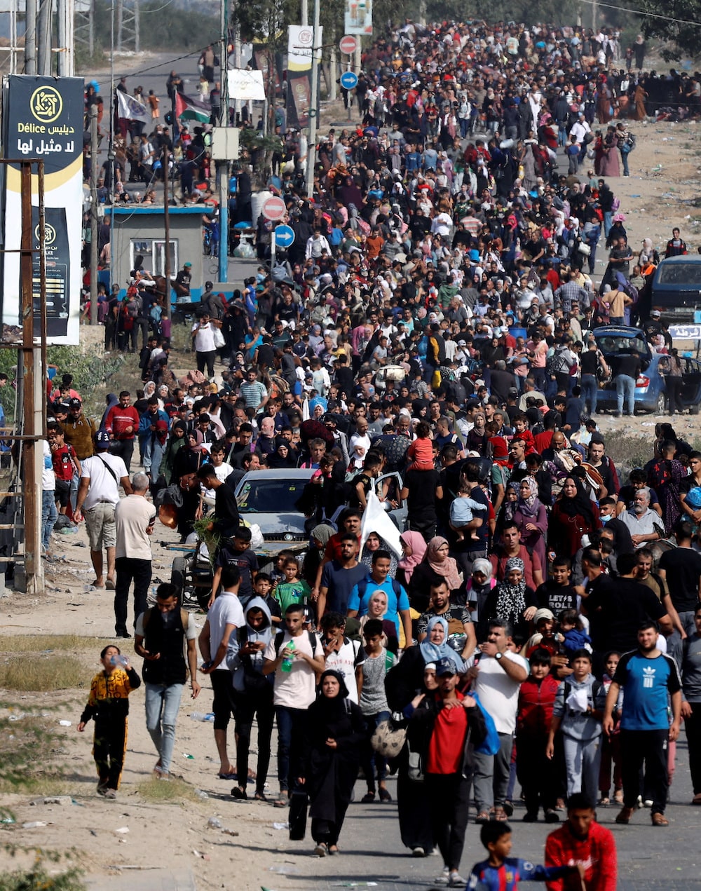 A long line of people walk along a road, many carrying bundles of belongings.