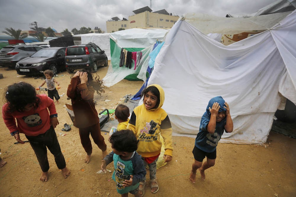 Children standing in the rain at a shelter in Deir al-Balah.