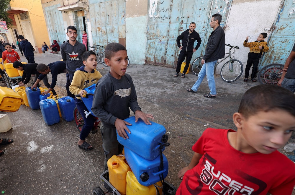 Palestinian children wait in a line with containers to collect water, amid drinking water shortages, in Rafah.