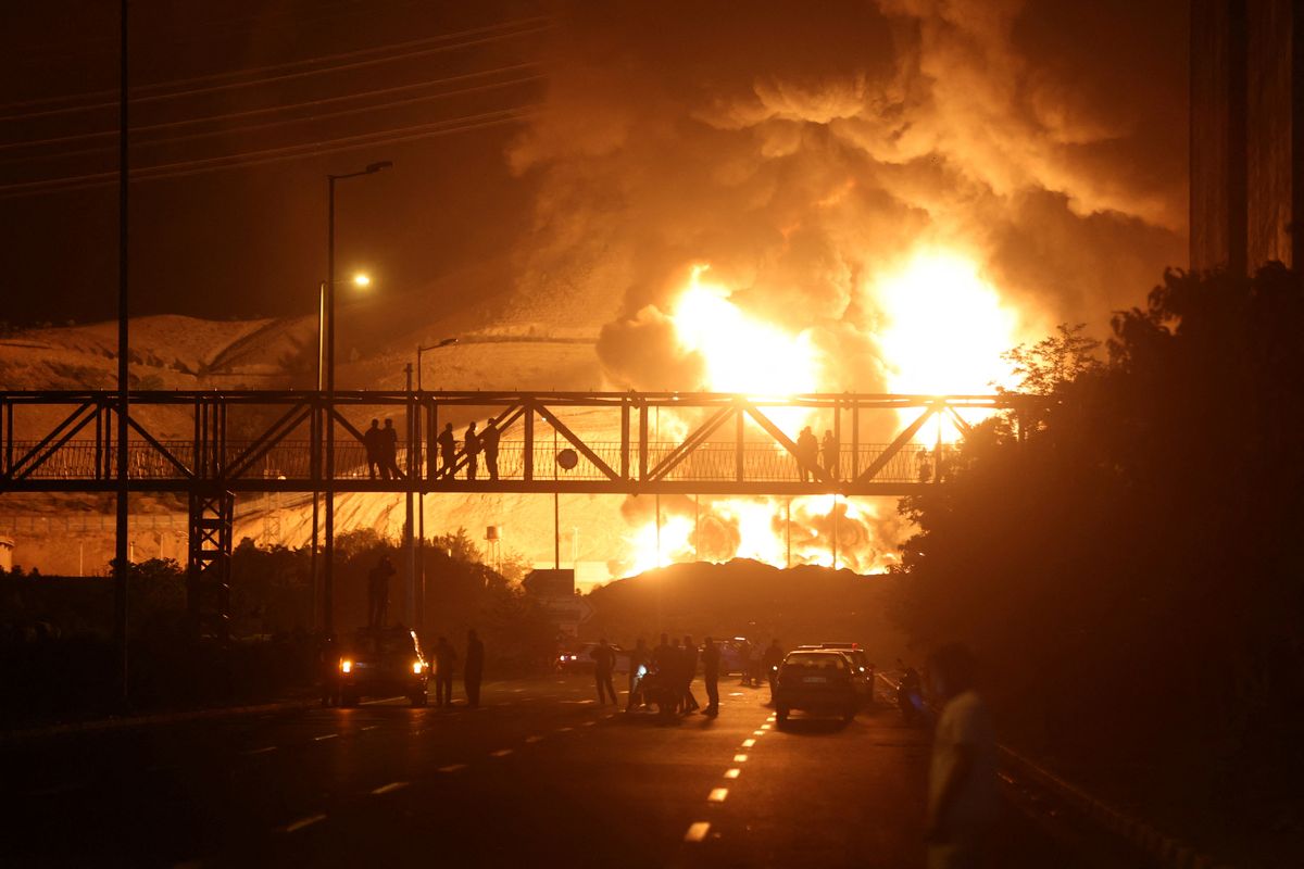People standing on a bridge observe flames and smoke rising from an oil depot following Israeli airstrikes in Tehran, Iran.